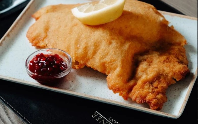 Das Original Wienerschnitzel auf hellem Teller mit Preiselbeeren und Zitrone