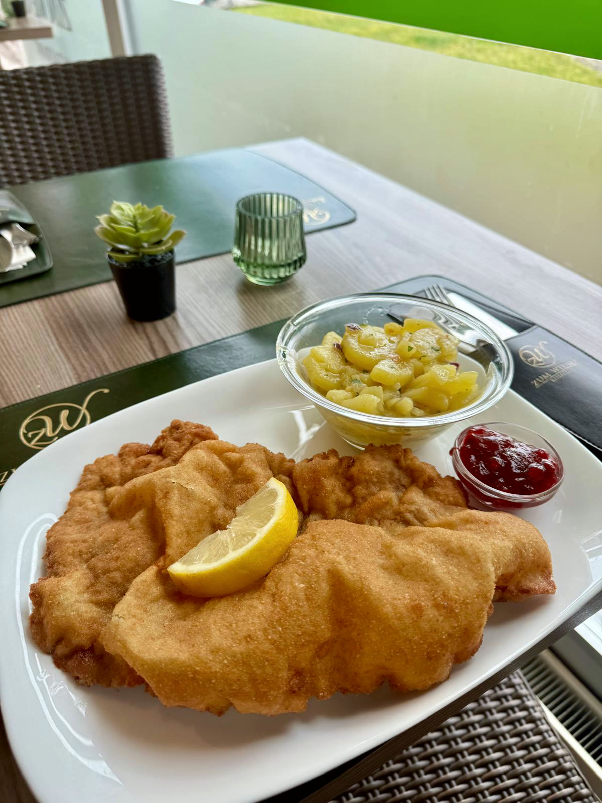 Wiener Schnitzel mit Kartoffelsalat und Preiselbeeren auf dem Tischset mit goldenem Zum-Wiener-Monogramm